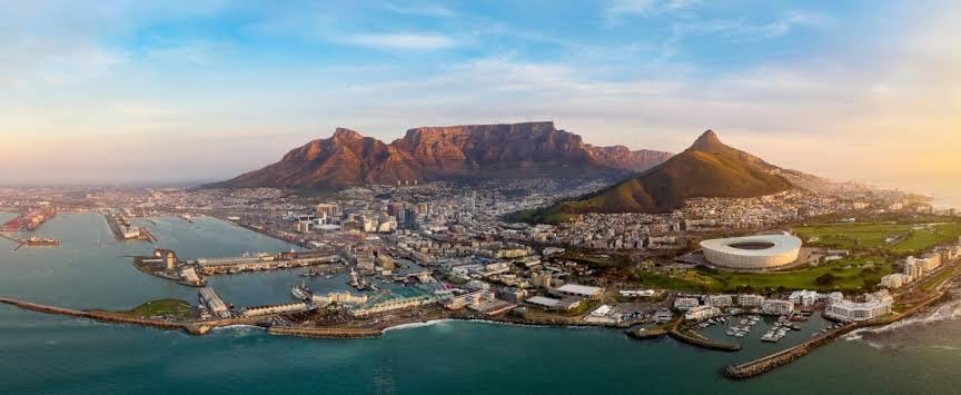 Aerial panoramic view of Cape Town at golden hour, with the V&A Waterfront harbour, Cape Town Stadium and city bowl below Table Mountain, featured in the Cape Town Long Weekend package